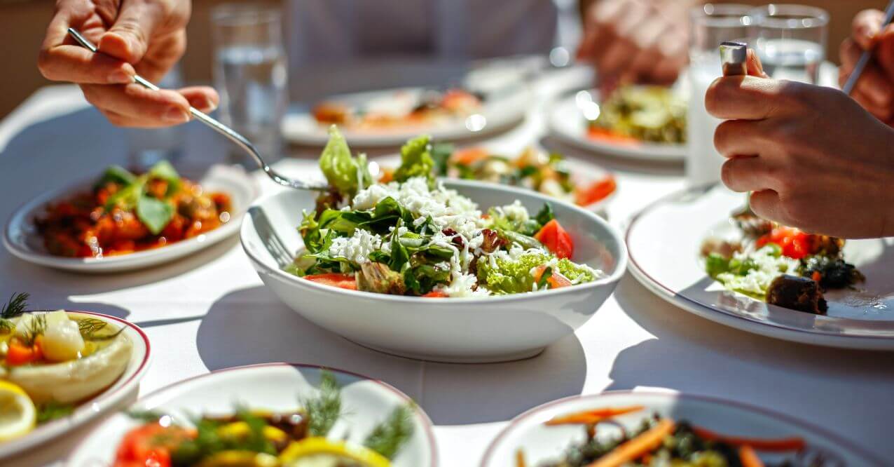 Hands serving salad from a central bowl, resembling 'What to Eat on a Parasite Cleanse'.